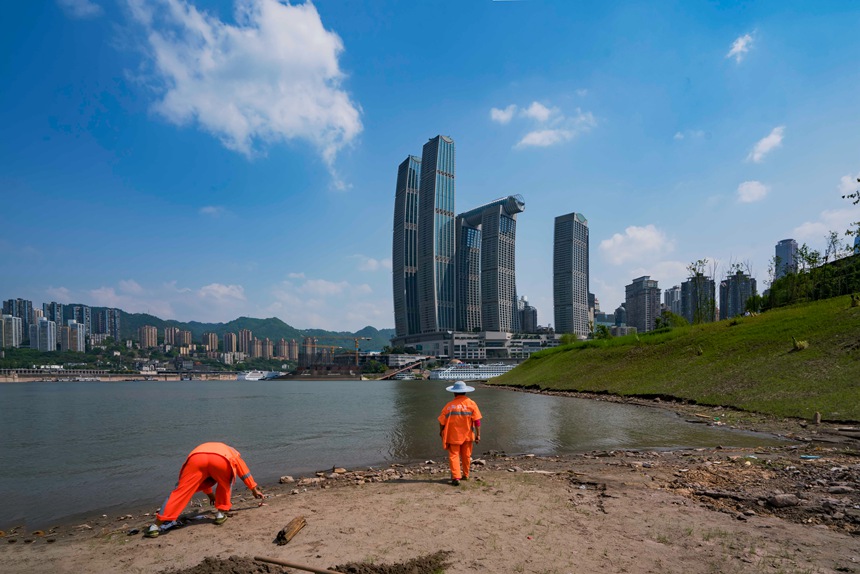 環衛工人冒著烈日清理河邊垃圾。黃進攝