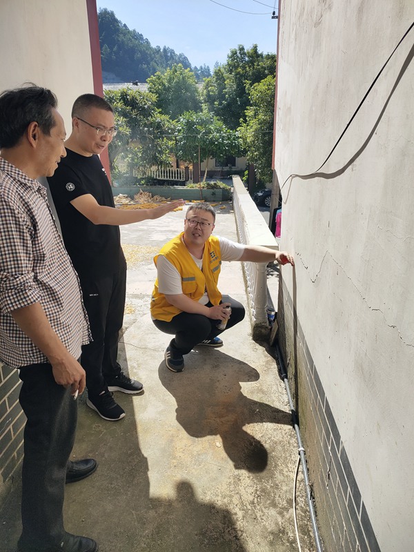 《炎炎夏日，地災巡查力度不減》。8月9日，107地質隊駐守隊員與沙壩鎮群測群防員頭頂烈日在萬慶村地質災害隱患點開展日常巡查，現場分析墻體裂縫形成的原因。路正昆攝