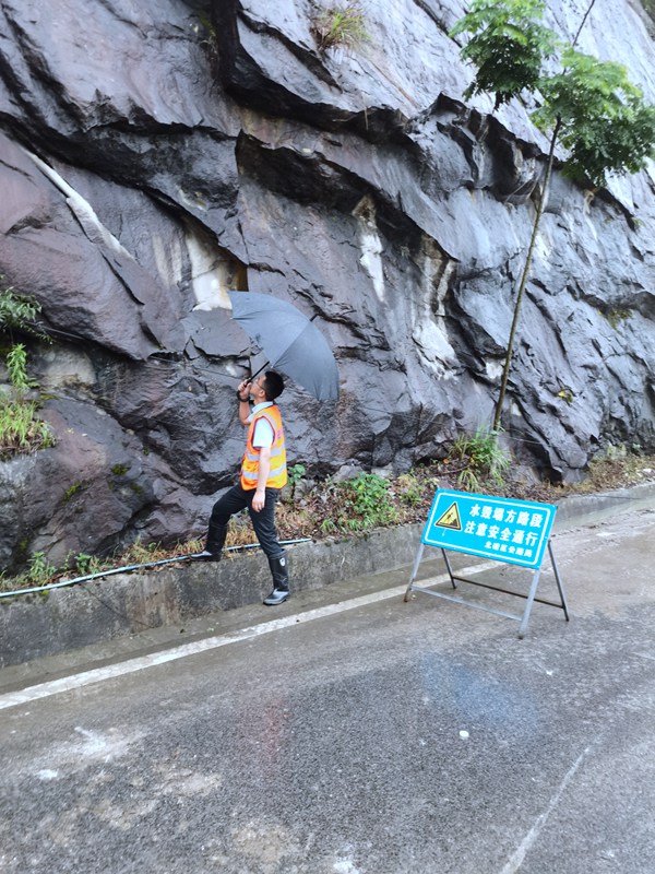 《看·守》。6月23日，208地質隊駐守隊員曹銳在北碚區天府鎮雨中巡查公路邊坡。