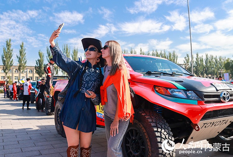 8月22日，外國游客在中國庫布齊沙漠越野賽暨中國汽車越野拉力錦標賽杭錦旗分站賽開幕式活動現場打卡留影。丁根厚攝