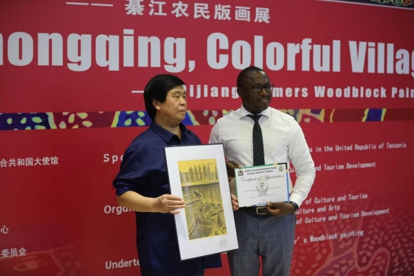 綦江農民版畫院院長桂煥勇手持楊榮作品《開放中的重慶》與坦桑尼亞國家博物館執行館長合影。重慶文藝職院供圖